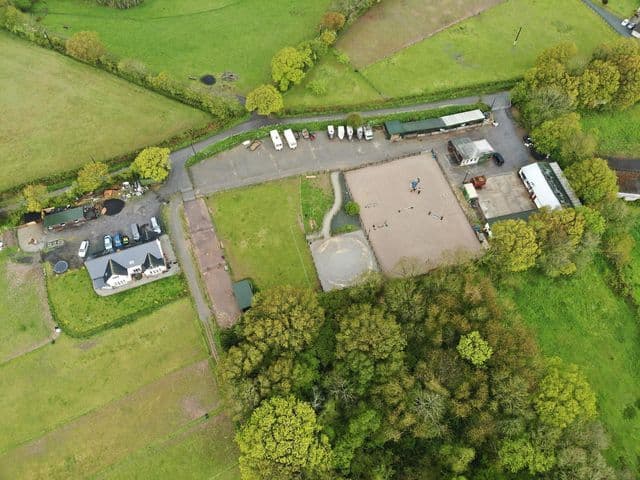 Drone aerial view of Blackdown Yard — barns, paddocks, arena and woodland surround.