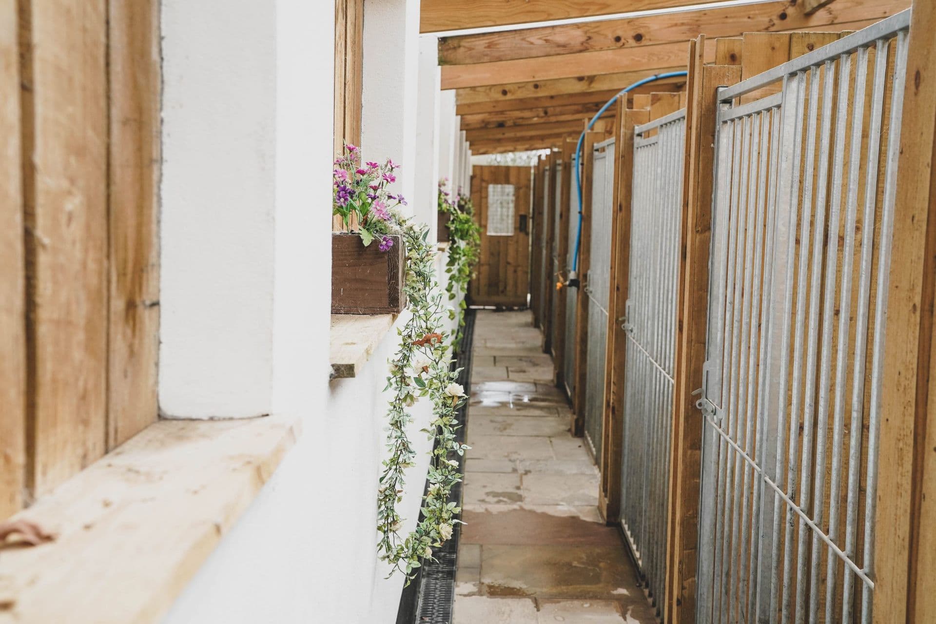 Outdoor stable corridor at Blackdown Yard with summer flower baskets along the eaves.